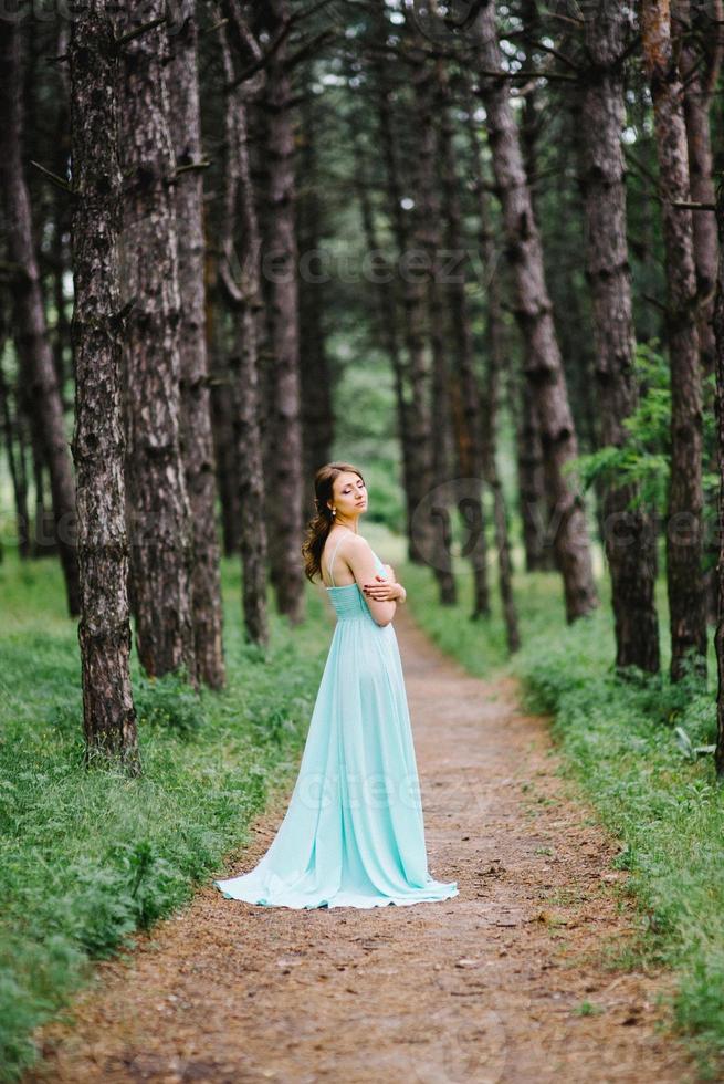 glückliches Mädchen in einem türkisfarbenen langen Kleid in einem grünen Park foto