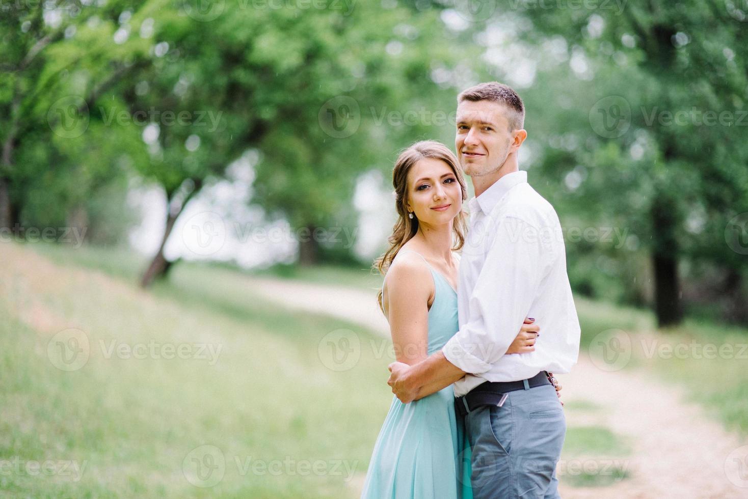 Ein glücklicher Kerl in einem weißen Hemd und ein Mädchen in einem türkisfarbenen Kleid gehen im Waldpark spazieren foto