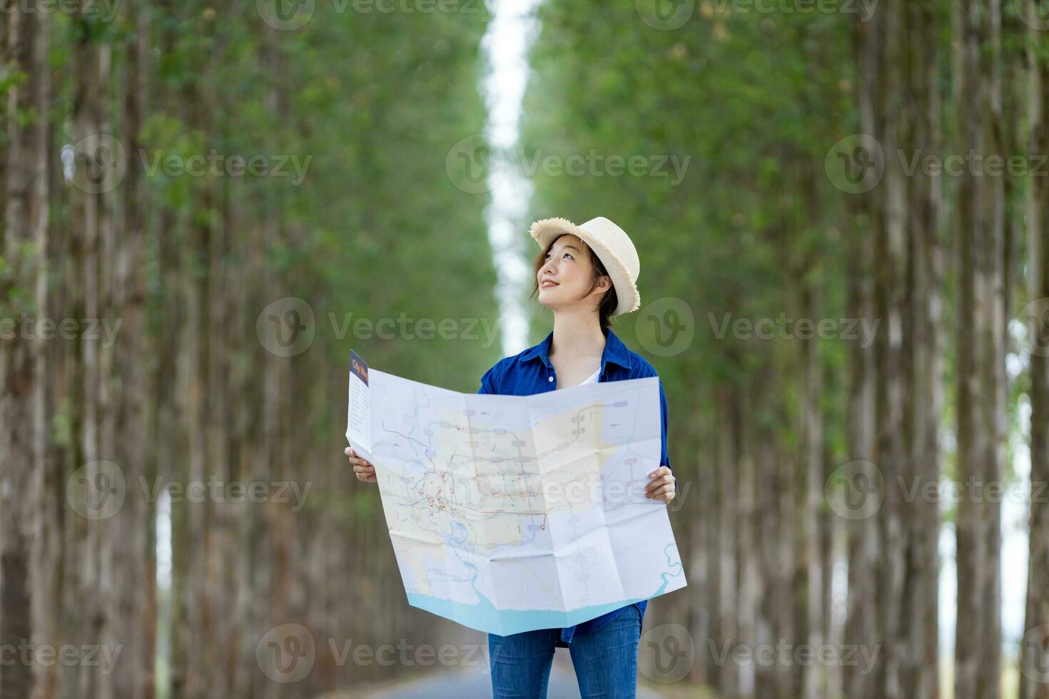 asiatisch Tourist Frau ist suchen beim das Karte zum Richtung während haben Ferien beim das National Park während Gehen auf das Straße mit Säule von Baum zum Reise und Abenteuer Konzept foto