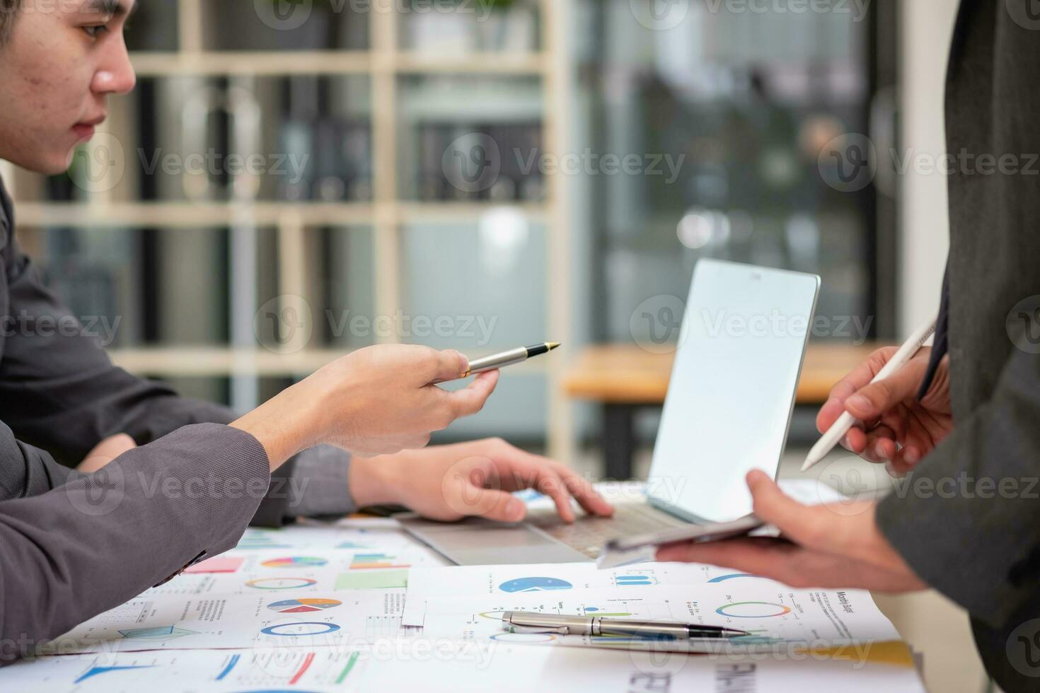 Das asiatische Geschäftsteam besteht aus Marketingmitarbeitern. Buchhalter und Finanzreferent helfen sich gegenseitig bei der Analyse von Unternehmensgewinnen mithilfe von Tablets. Taschenrechner-Laptops, Millimeterpapier und Firmenkugelschreiber. foto