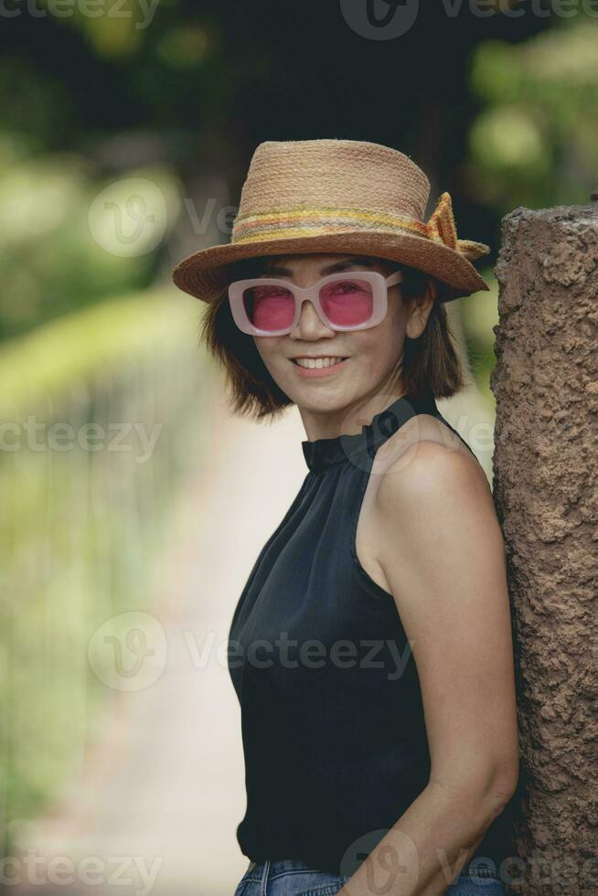 ziemlich Frau tragen Stroh Hut zahnig lächelnd mit Glück Stehen draussen foto