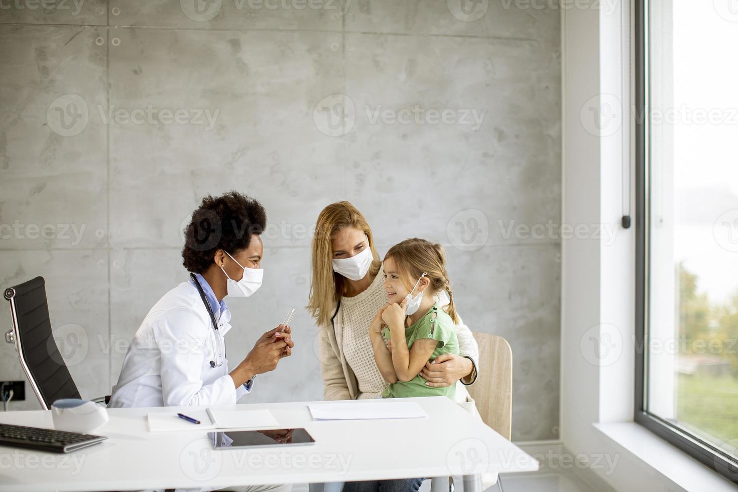 Kinderarzt untersucht kleines Mädchen mit anwesenden Eltern foto