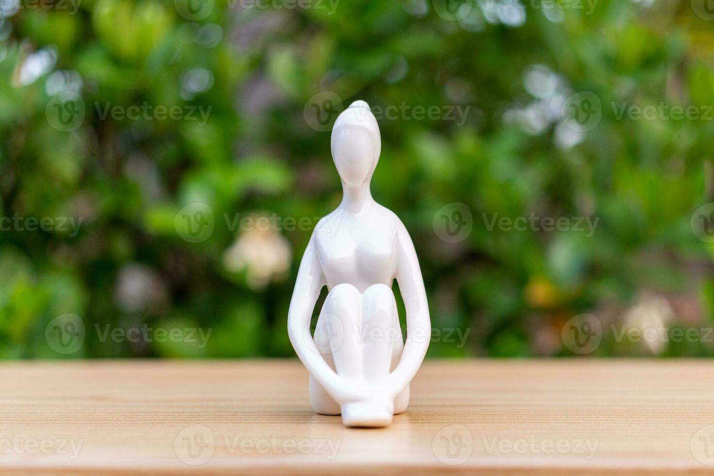 Keramik Yoga Figur von Frau tun Yoga Pose auf hölzern Fußboden und Grün Blatt Hintergrund foto