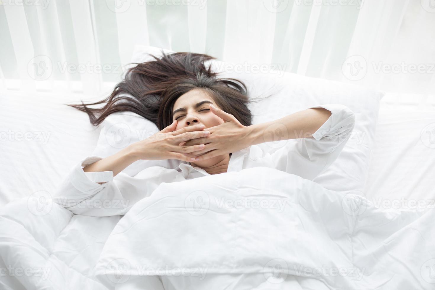 Frau gähnt im weißen Bett foto