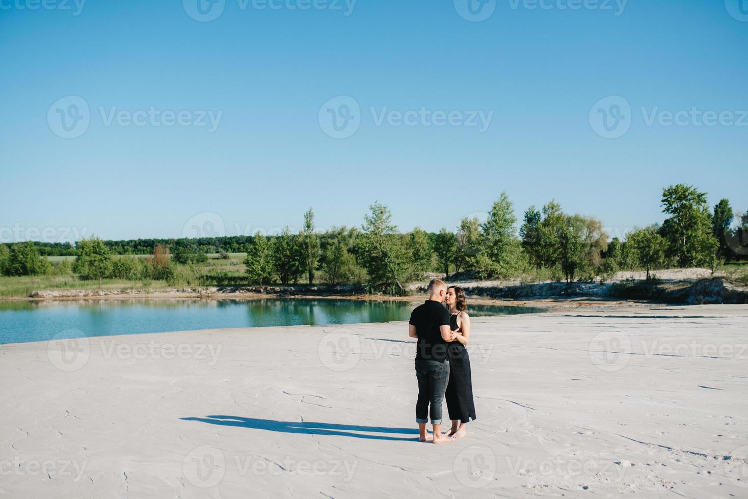 junges Paar ein Mann mit einem Mädchen in schwarzen Kleidern geht auf dem weißen Sand foto