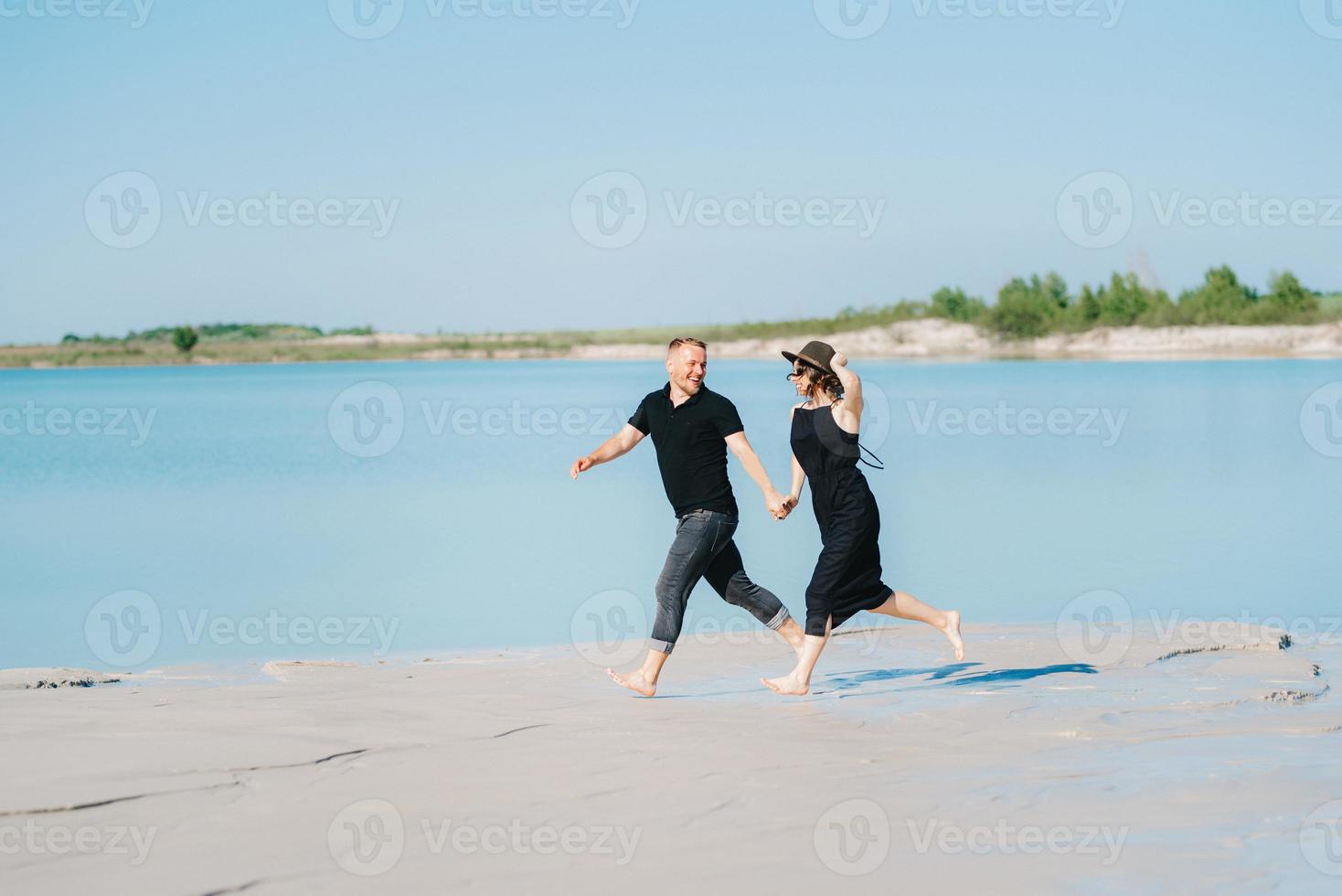 junges Paar ein Mann mit einem Mädchen in schwarzen Kleidern geht auf dem weißen Sand foto