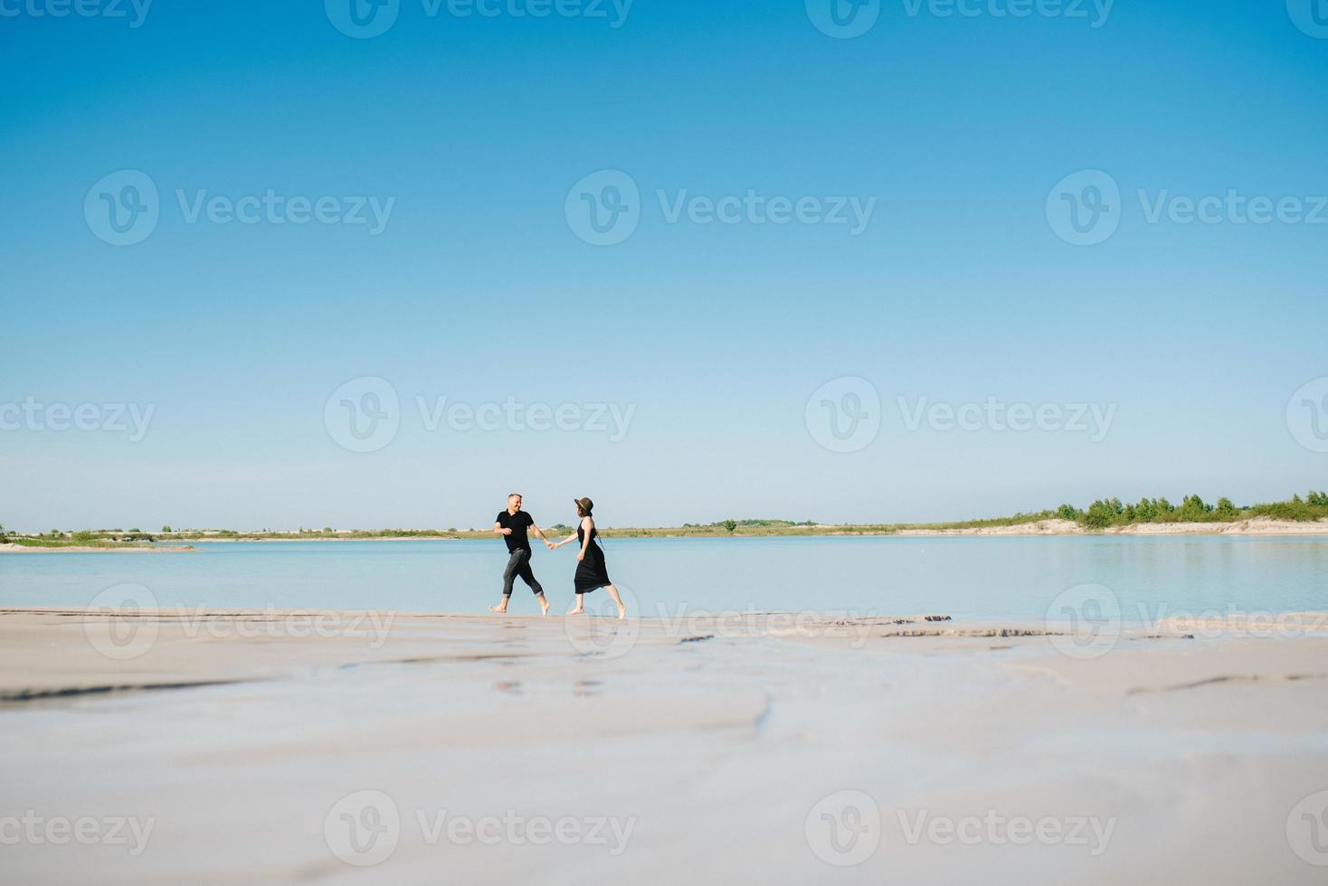 junges Paar ein Mann mit einem Mädchen in schwarzen Kleidern geht auf dem weißen Sand foto