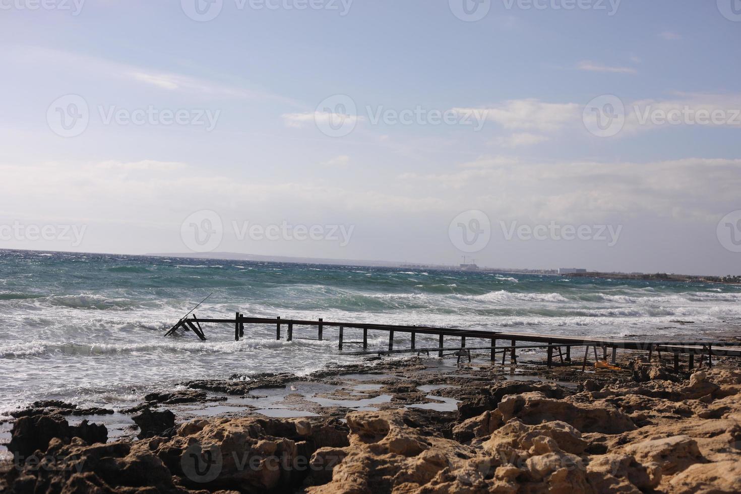 Steinstrand mit altem hölzernen Ponton nahe dem Meereshintergrund foto