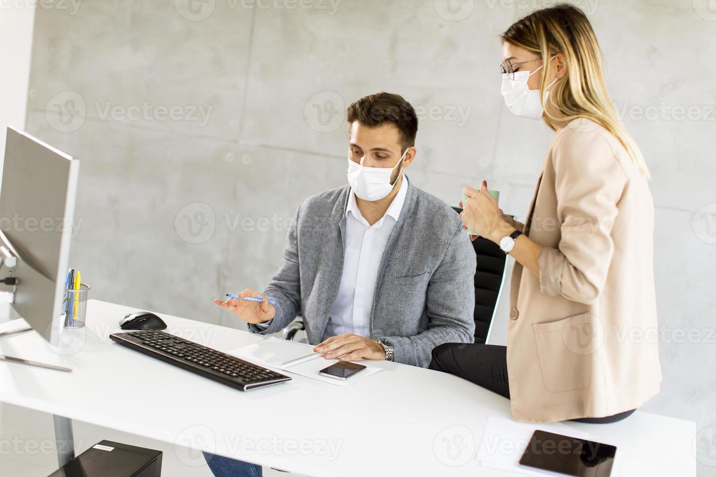 Geschäftsleute, die am Schreibtisch in Masken arbeiten foto