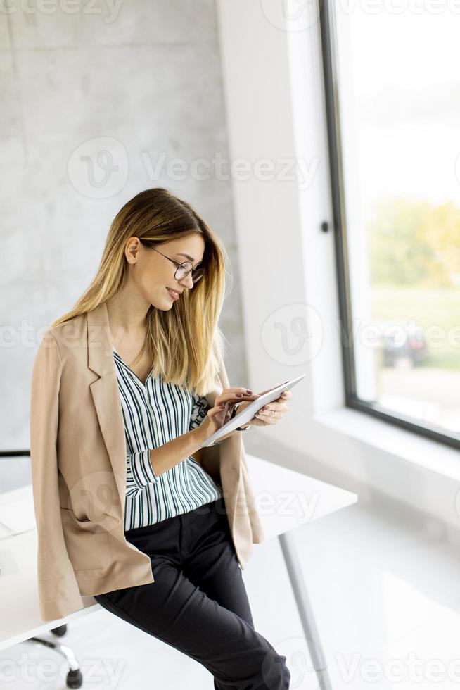 Geschäftsfrau, die auf der Kante eines Schreibtisches mit einem Tablett sitzt foto
