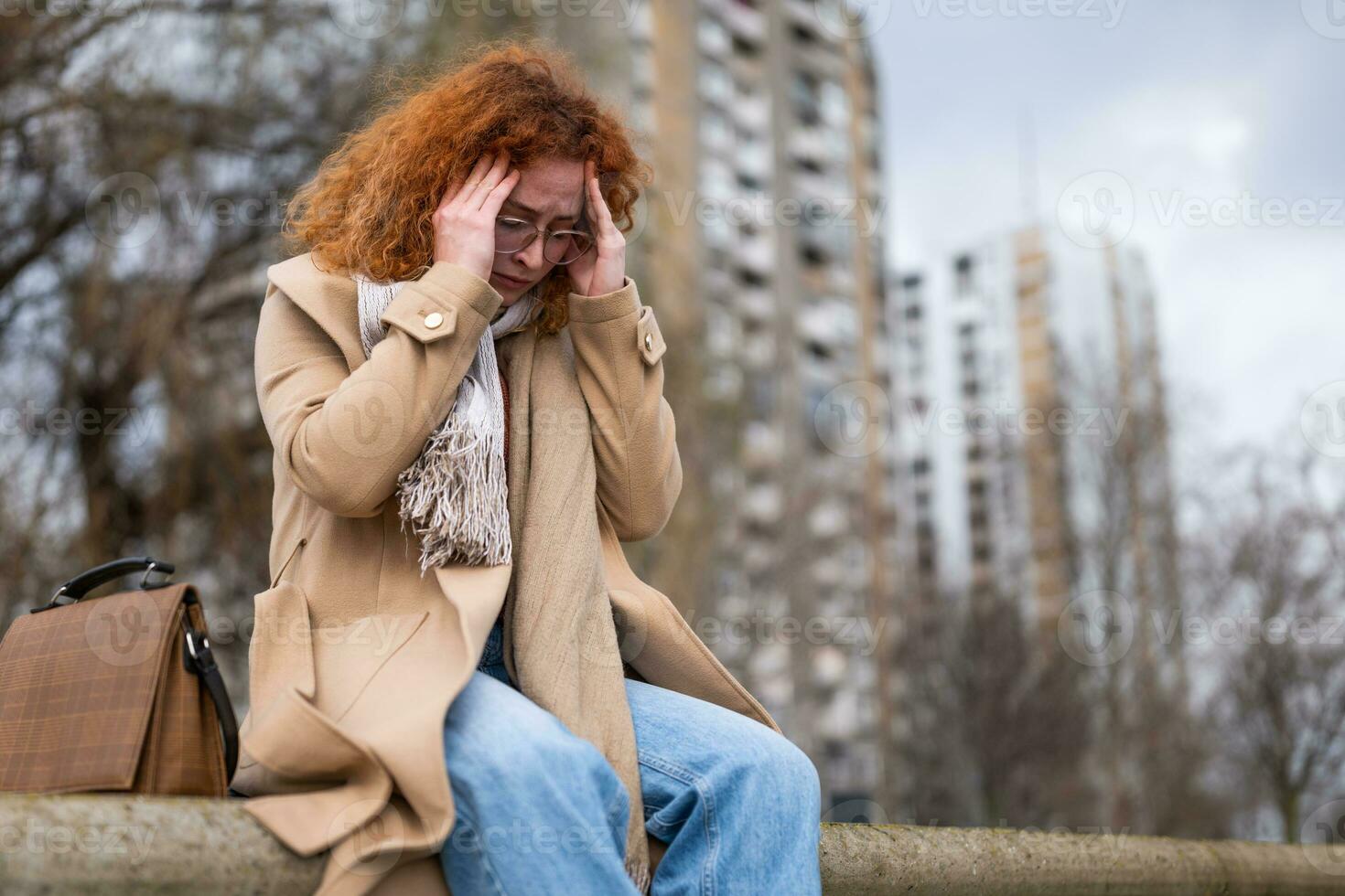 kaukasisch Ingwer Frau mit lockig Haar ist Sitzung draussen im das Stadt. sie ist müde und haben Kopfschmerzen. foto