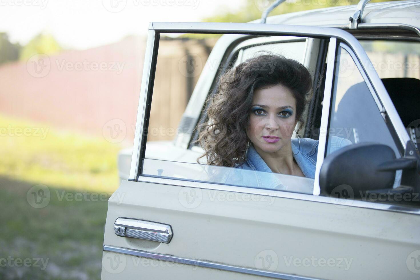 komisch jung Frau im ein Denim Jacke mit bilden im das Stil von das achtziger Jahre sieht aus durch das Auto Fenster. foto