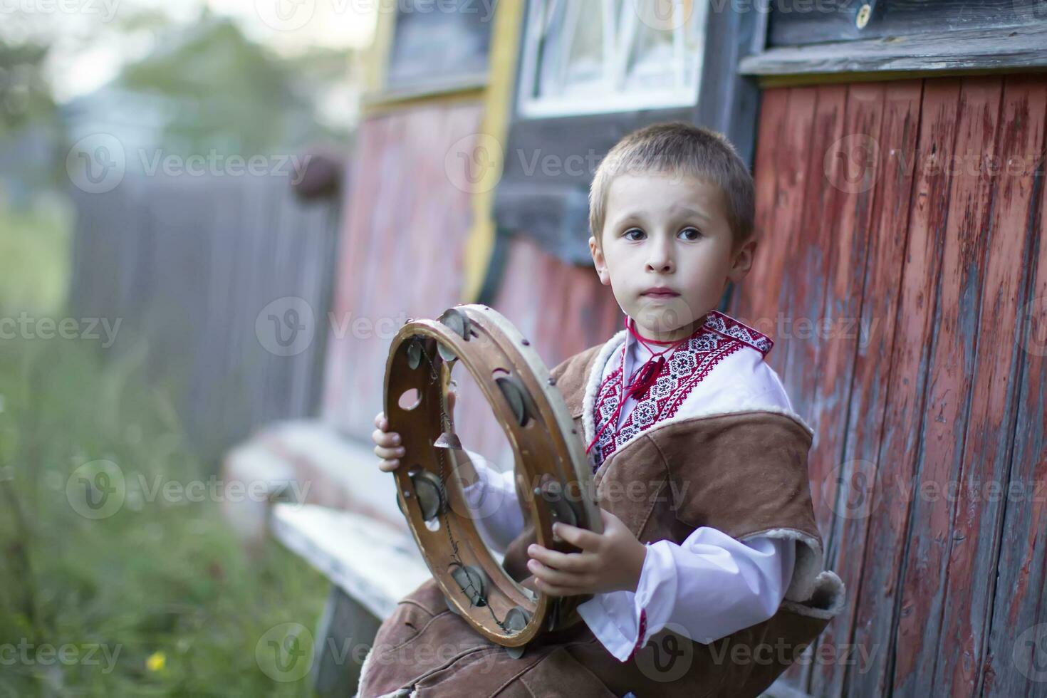 wenig Junge im slawisch National Kleid mit ein ethnisch Tambourin. ein Belarussisch oder ukrainisch Kind im ein gestickt Hemd mit ein Volk Musical Instrument. foto