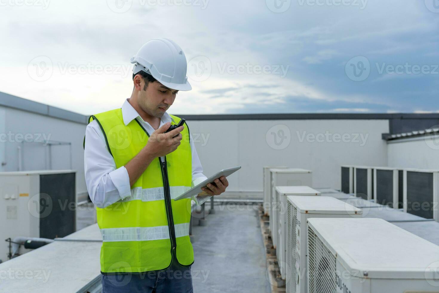 asiatisch Instandhaltung Ingenieur funktioniert auf das Dach von Fabrik. Auftragnehmer prüfen Kompressor System und Pläne Installation von Luft Bedingung Systeme im Konstruktion. Technologie, online, Handy, Mobiltelefon Anwendung. foto