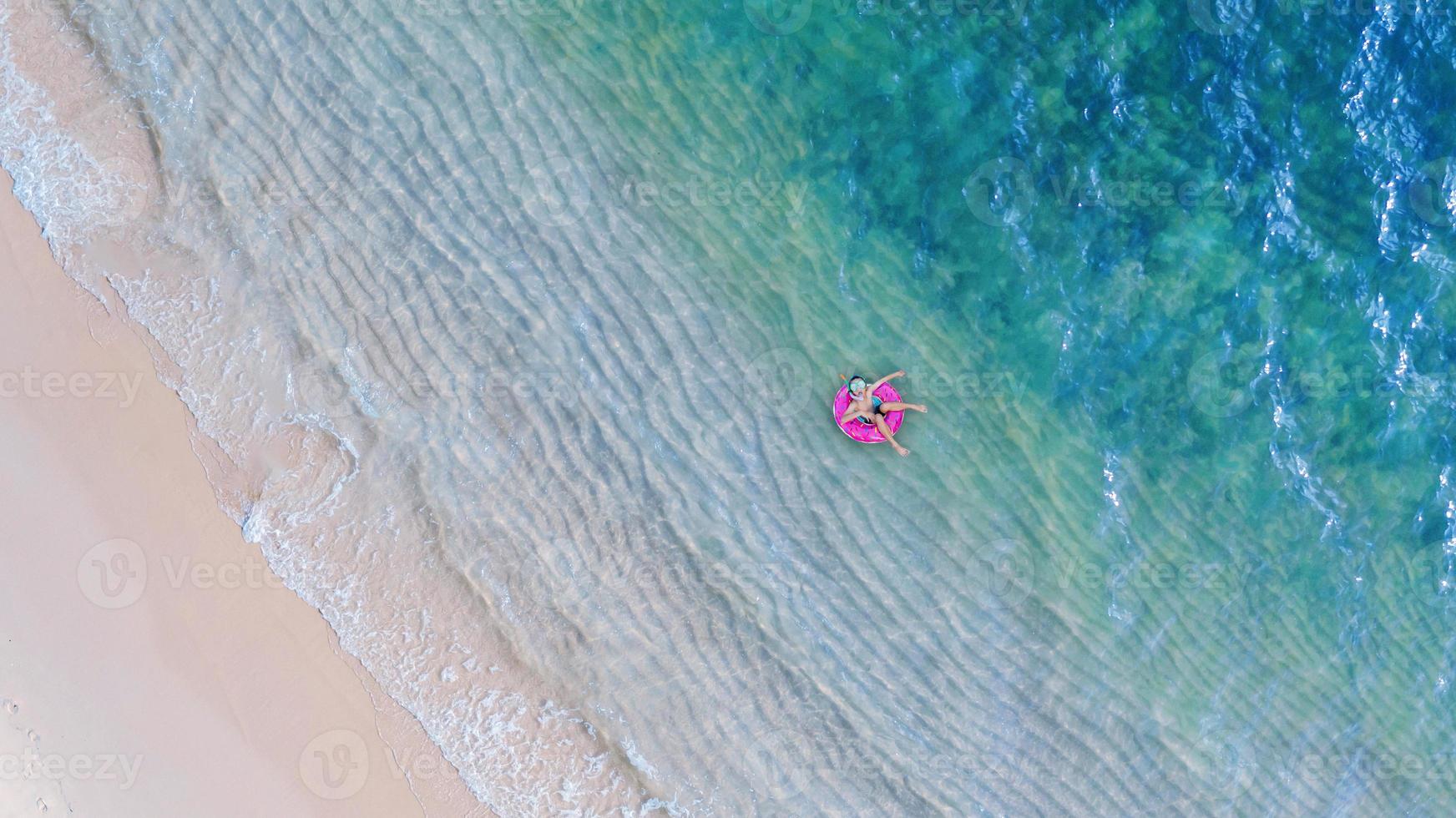 Luft Draufsicht von der Drohnenansicht des Jungen mit Schwimmring im Meer und Schatten smaragdblauem Wasser und Wellenschaum bei Sonnenaufgang foto