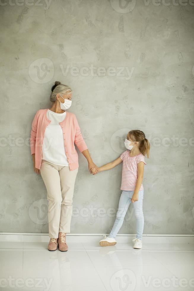 Großmutter hält die Hand der Enkelin und trägt Masken foto