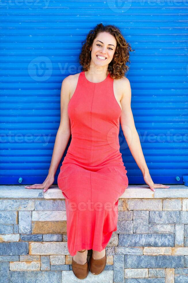 glücklich Frau im rot Kleid Sitzung auf Stein Mauer foto