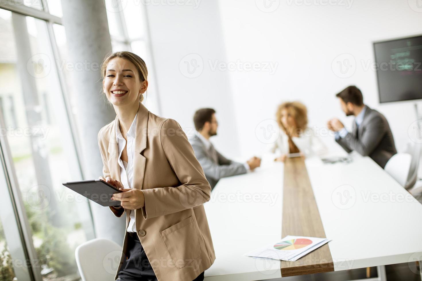 Geschäftsfrau, die eine Tafel mit einer Besprechung im Hintergrund hält foto