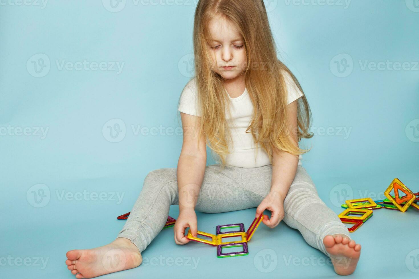 wenig Mädchen spielen mit bunt magnetisch Konstrukteur Spielzeug auf Blau Hintergrund foto