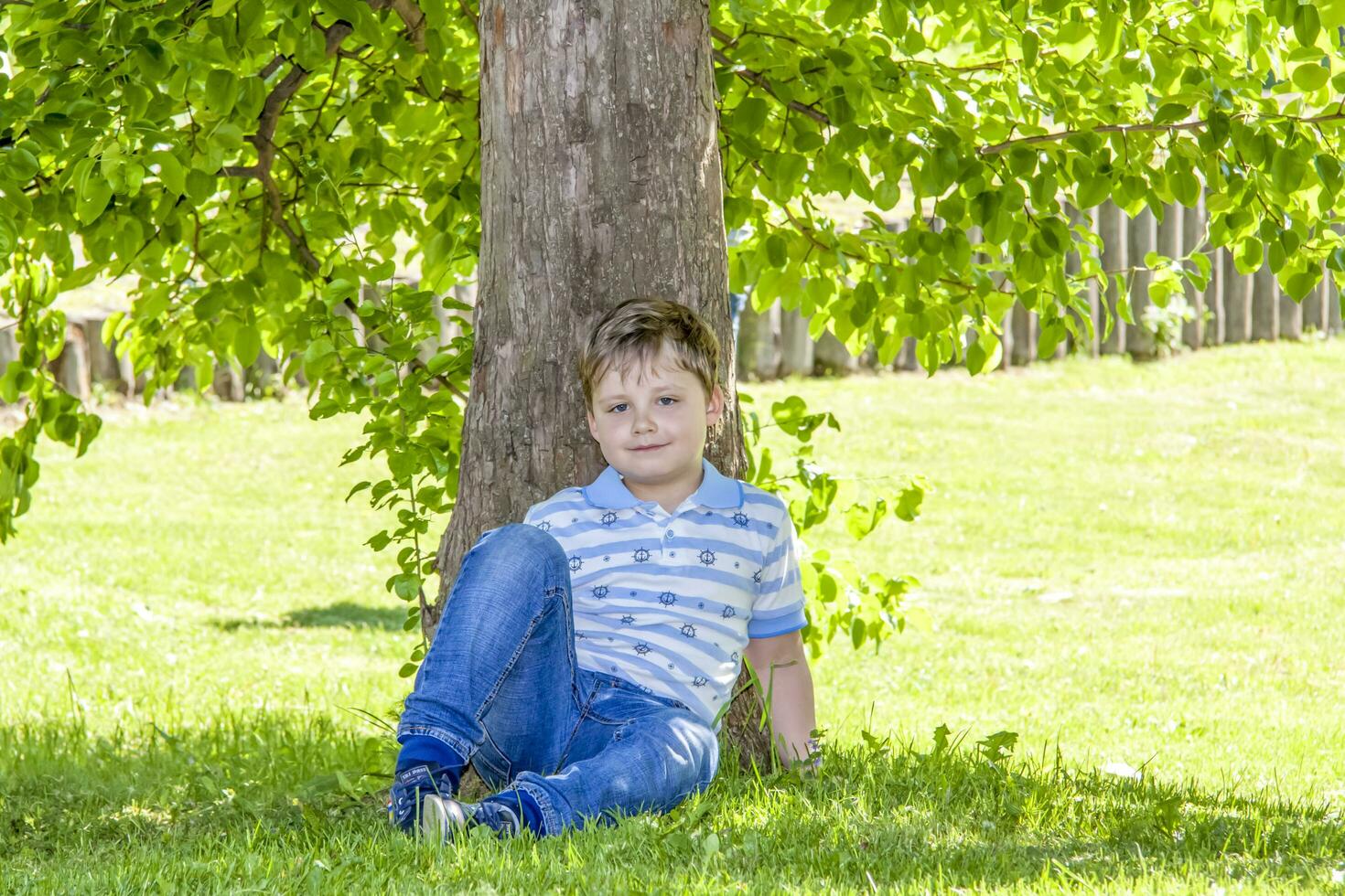 das Junge ist Sitzung im das Schatten unter ein Baum. versteckt von das Sonne foto