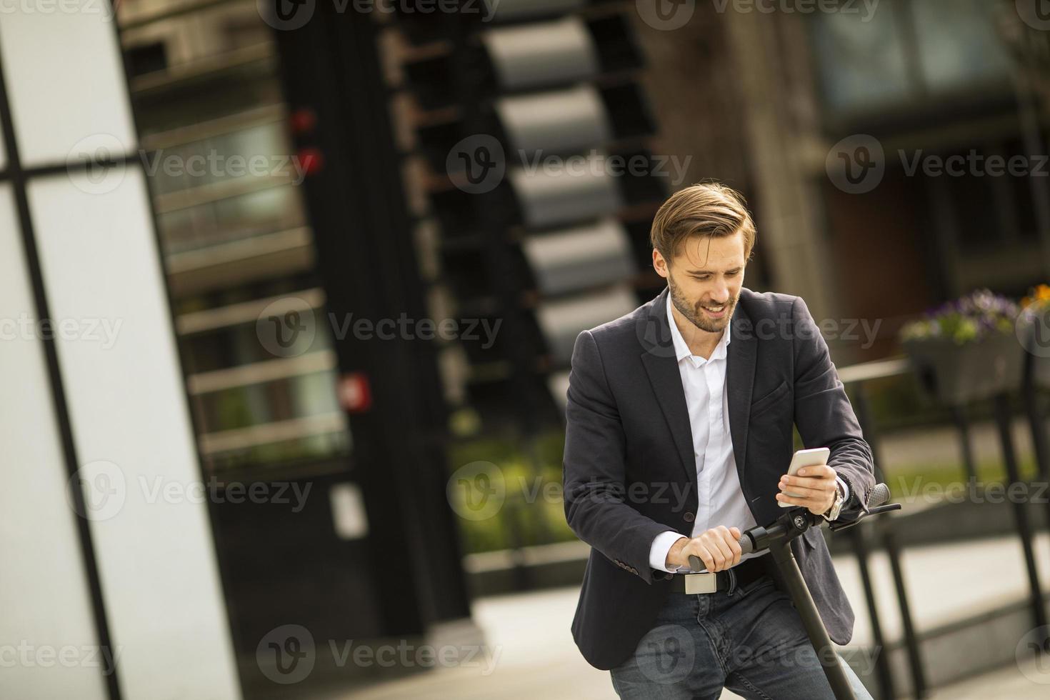Geschäftsmann, der Telefon auf einem Roller betrachtet foto