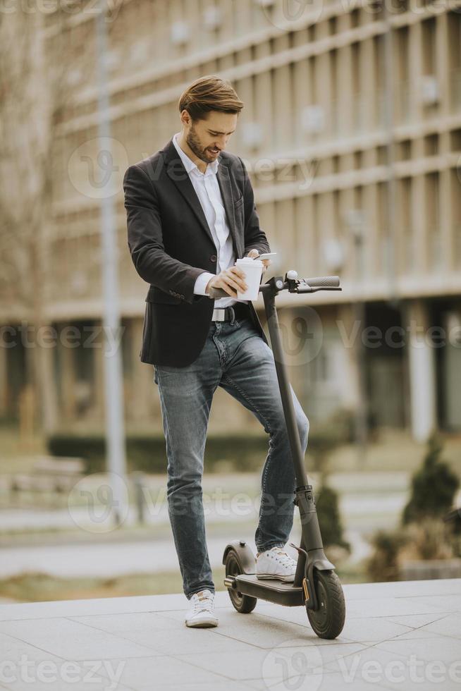 Gelegenheitsgeschäftsmann, der einen Kaffee hält und SMS auf einem Roller foto