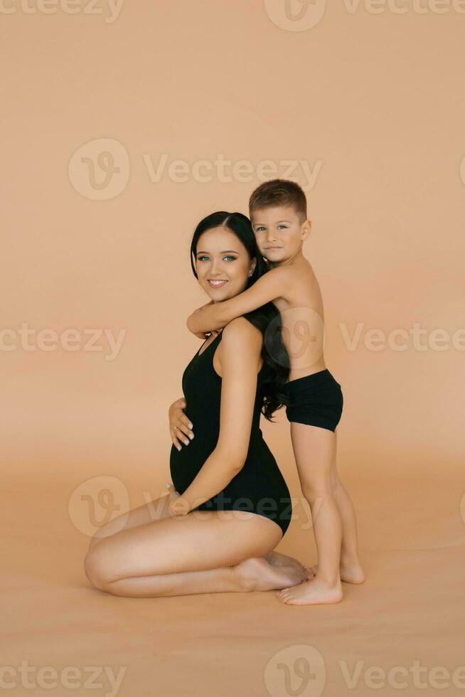 Porträt von ein schön glücklich schwanger Frau und ihr süß Baby, isoliert Bild auf ein Beige Hintergrund foto