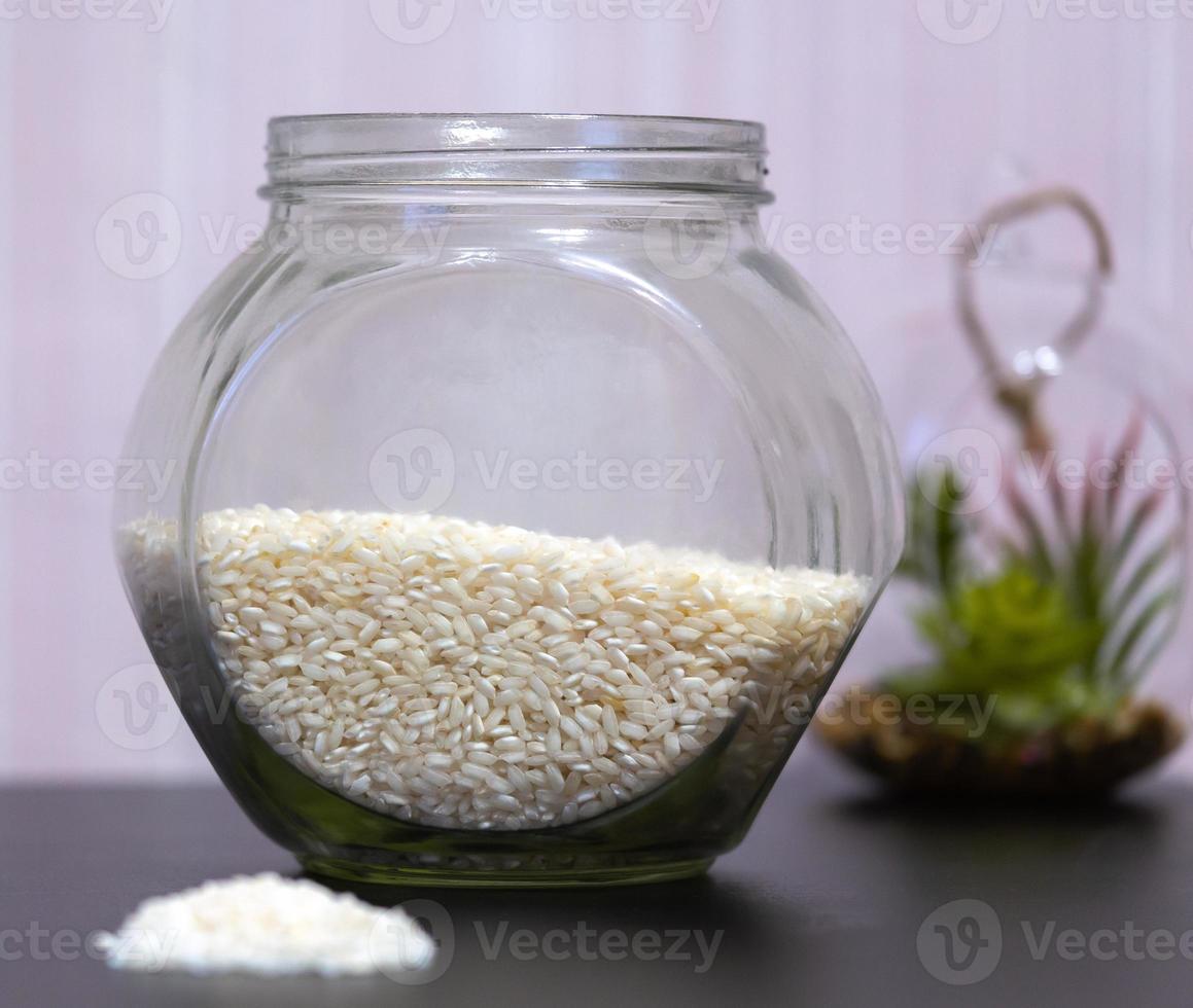 Reis in einem Glas, das auf einem Tisch mit einer grünen Pflanze im Hintergrund steht foto