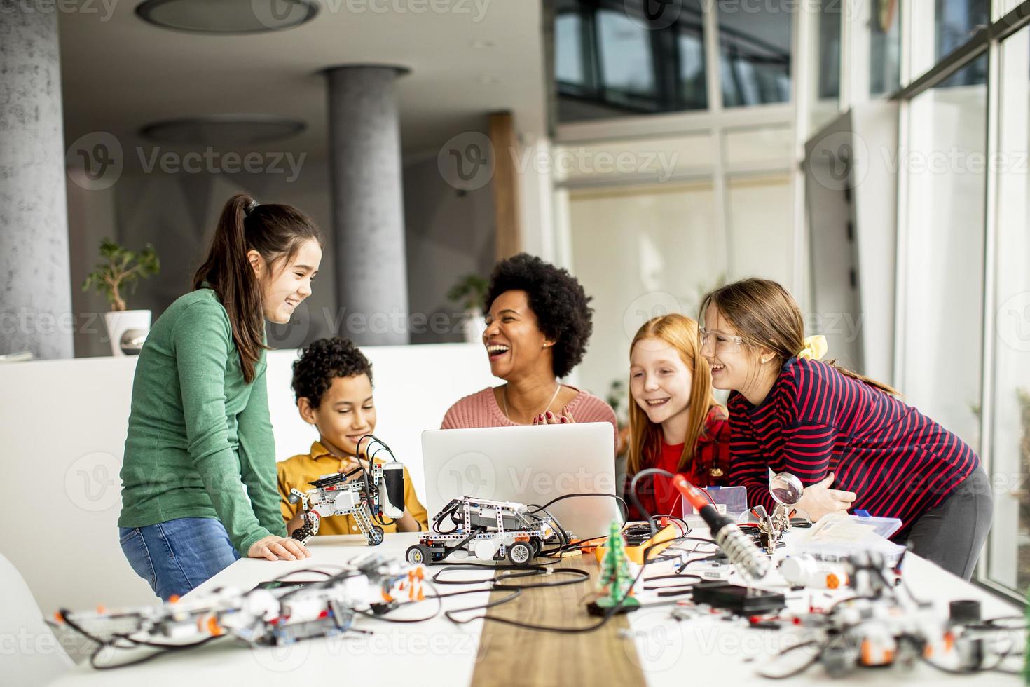 glückliche Kinder mit ihrer afroamerikanischen Wissenschaftslehrerin mit Laptop-Programmierung von elektrischem Spielzeug und Robotern im Robotik-Klassenzimmer foto