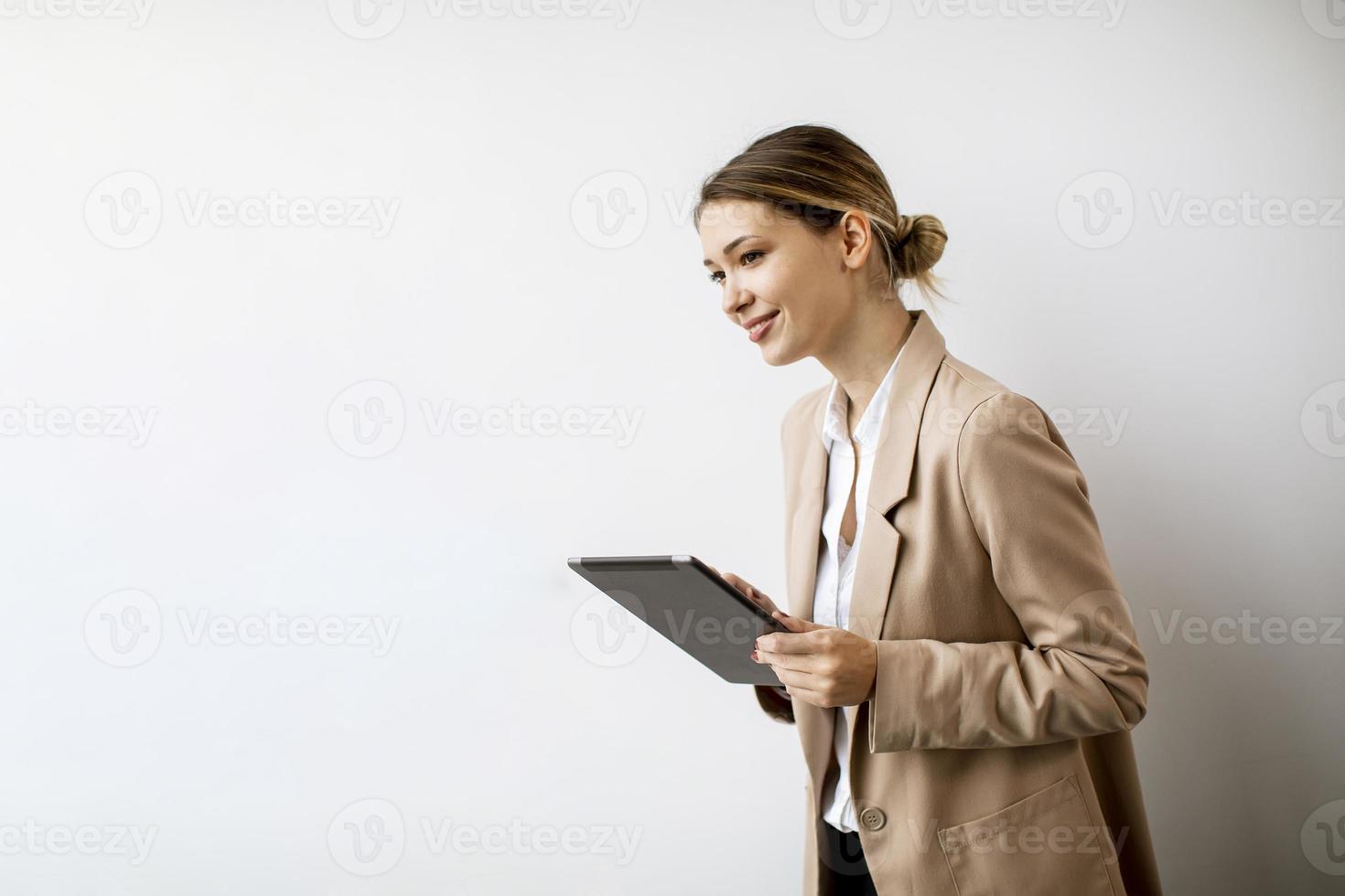 junge Frau, die digitales Tablett durch die weiße Wand im modernen Büro hält foto