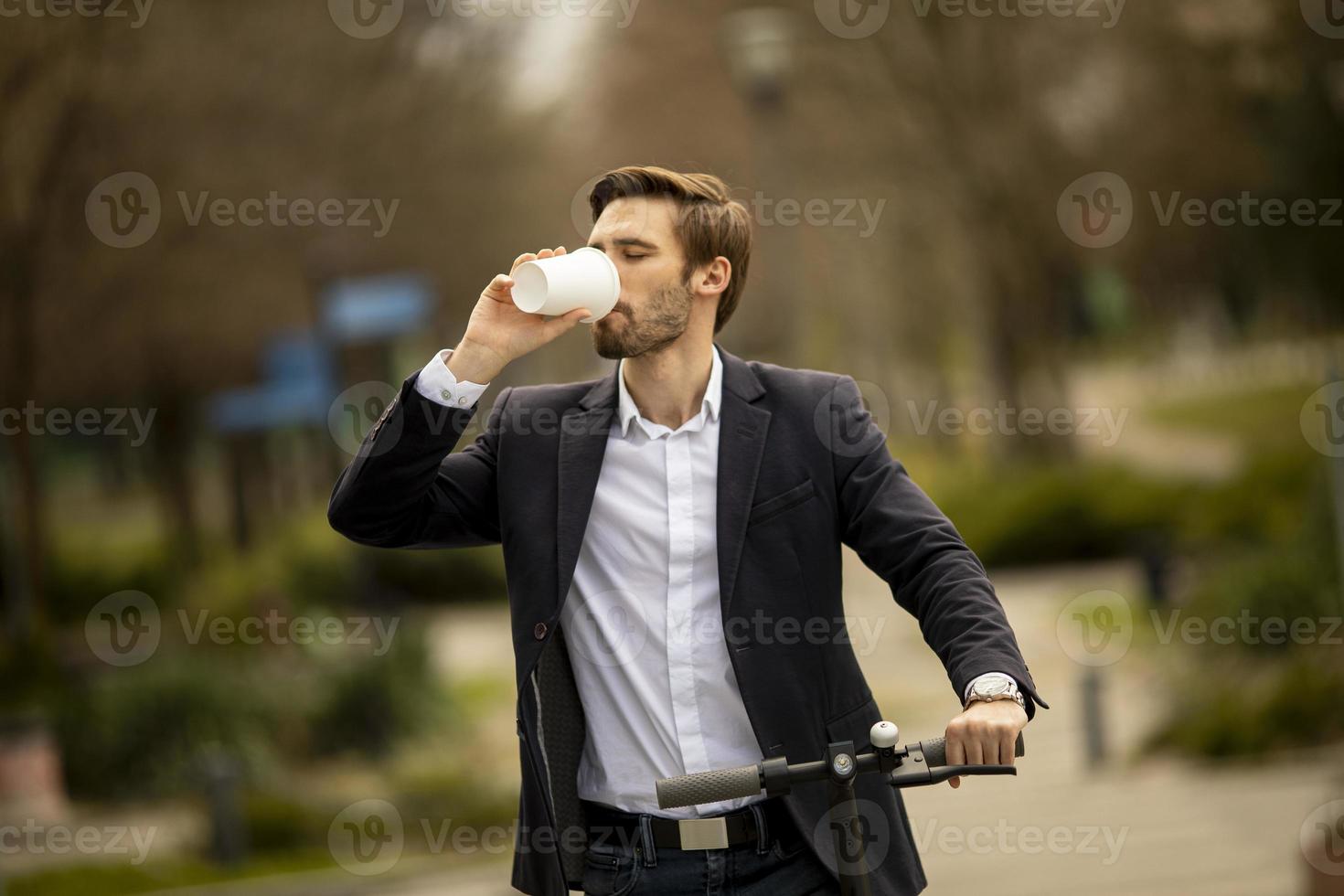 junger Geschäftsmann mit Kaffeetasse zum Mitnehmen auf Elektroroller foto