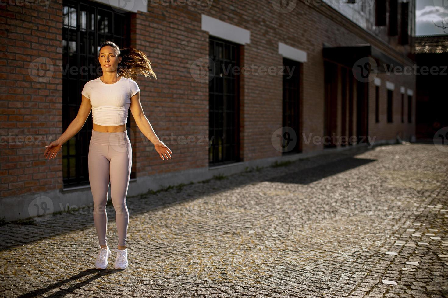 junge Frau, die sich während des Trainings in der städtischen Umgebung ausdehnt foto