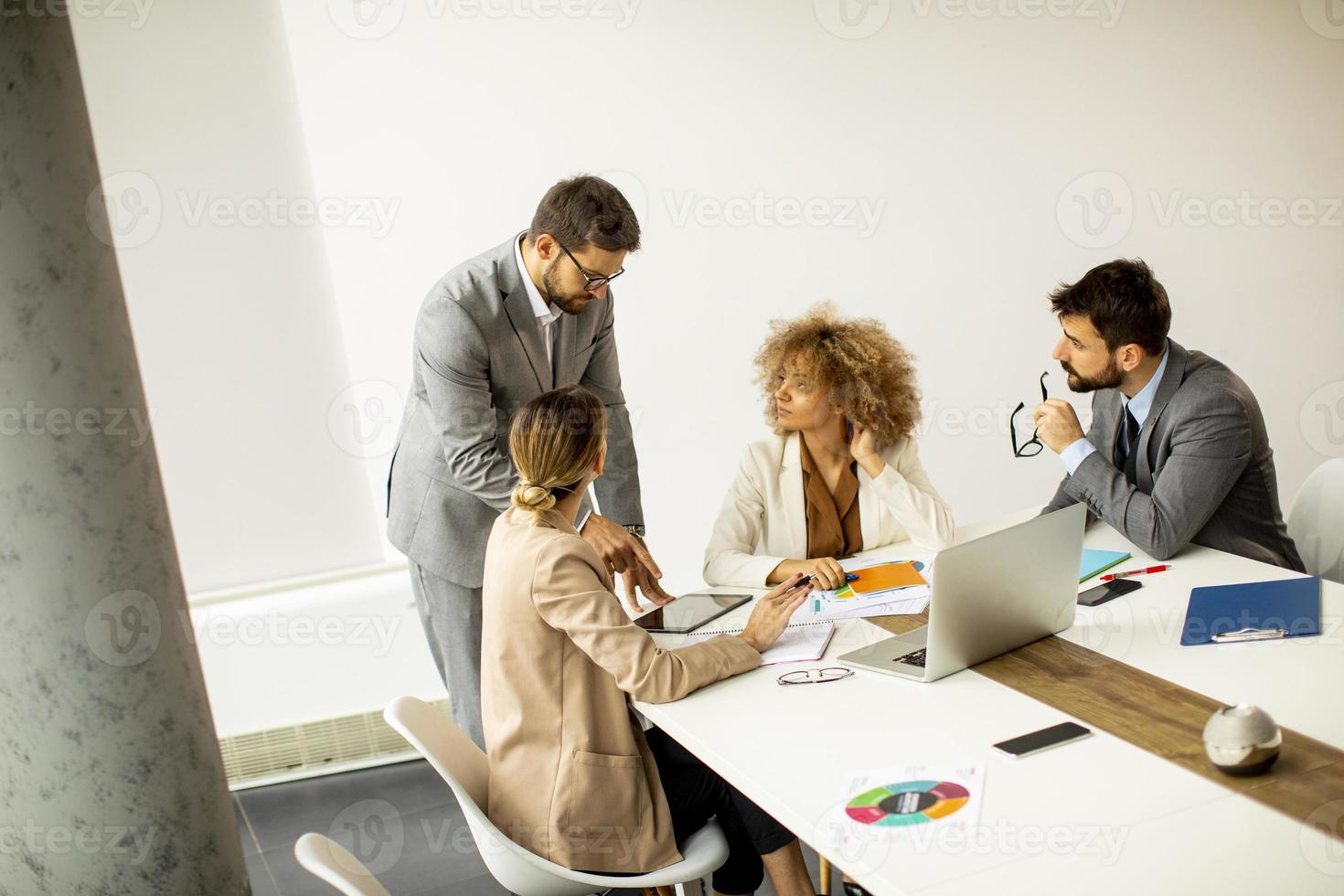 Gruppe junger Geschäftsleute, die arbeiten und kommunizieren, während sie zusammen am Schreibtisch sitzen foto