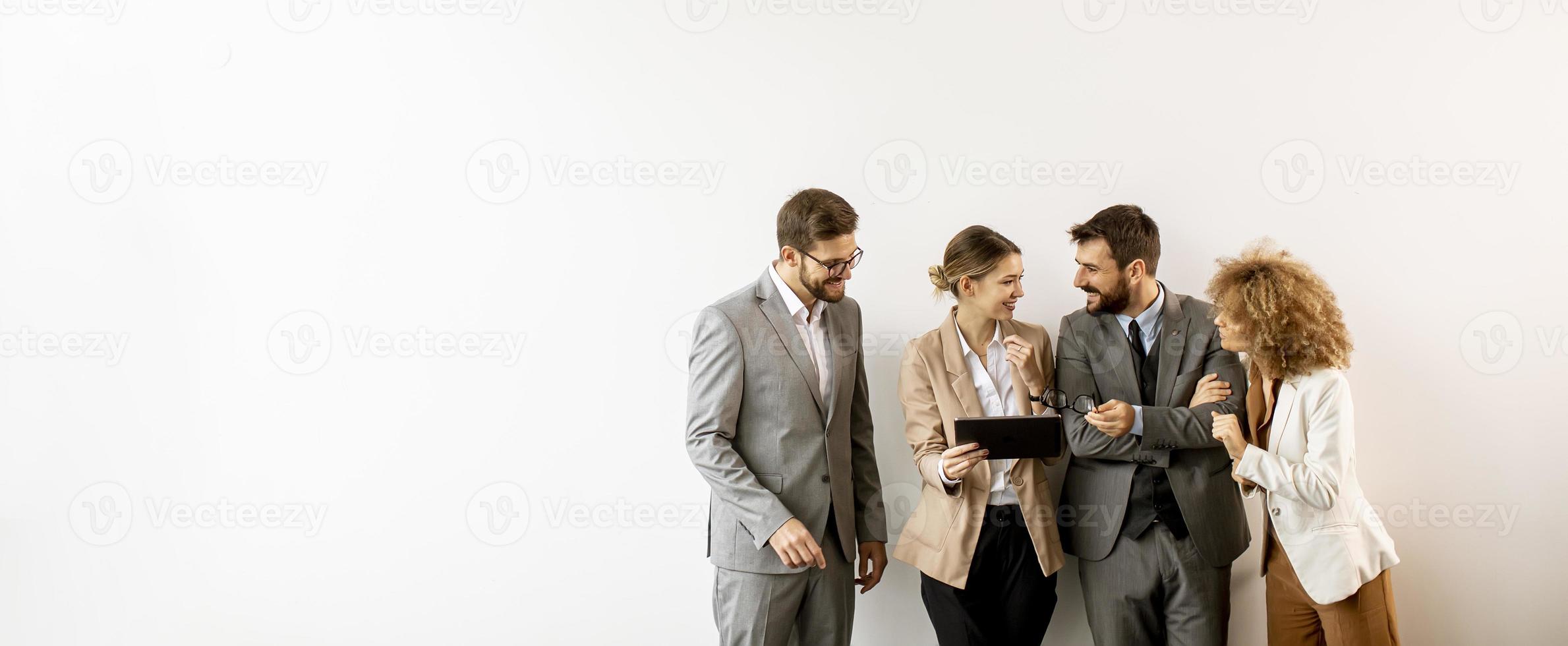 Multiethnische Geschäftsleute, die digitales Tablet verwenden, während sie an der Wand im Büro stehen foto