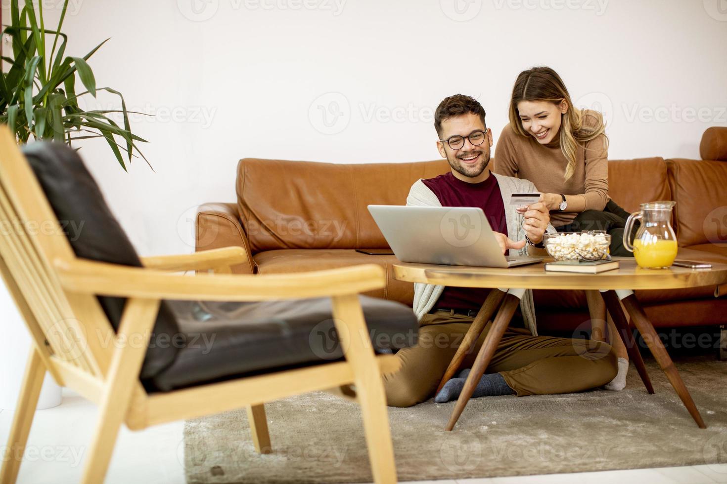 junge Frau und junger Mann, die Laptop für Online-Zahlung verwenden, während sie zu Hause am Sofa sitzen foto