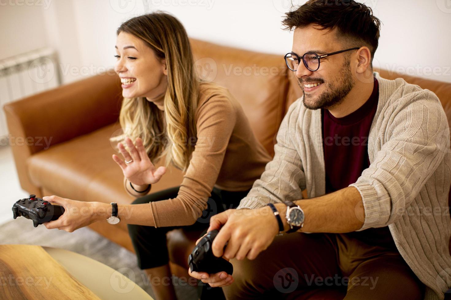 junges Paar, das zu Hause Videospiele spielt, auf Sofa sitzt und sich amüsiert foto