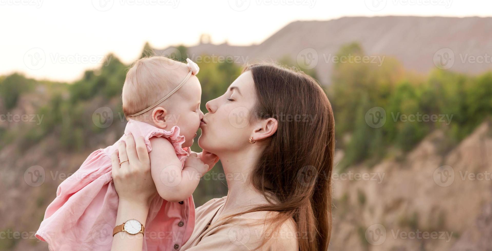 Mutter hält ein Kind in den Armen und küsst es im Freien sanft auf die Wange foto