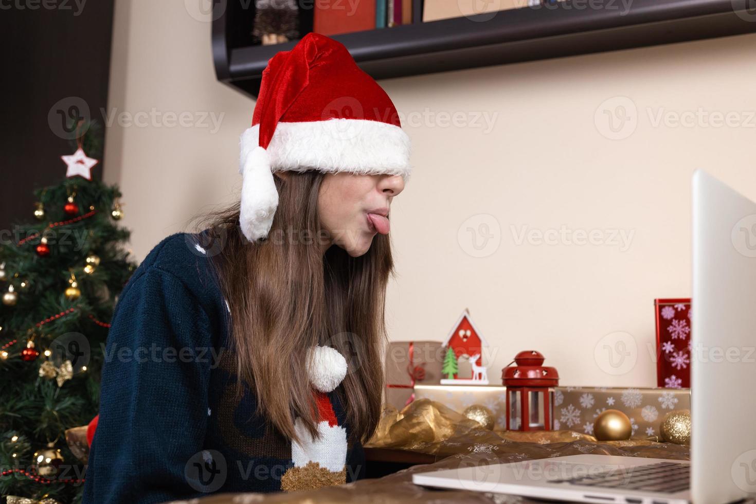 Mädchen im Weihnachtsmannhut mit Laptop für Videoanruf an Freunde und Eltern foto