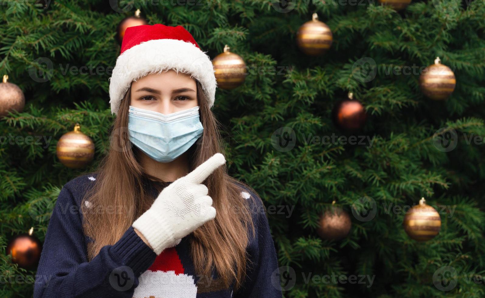 Nahaufnahmeporträt der Frau, die einen Weihnachtsmannhut und eine medizinische Maske mit Emotion trägt foto