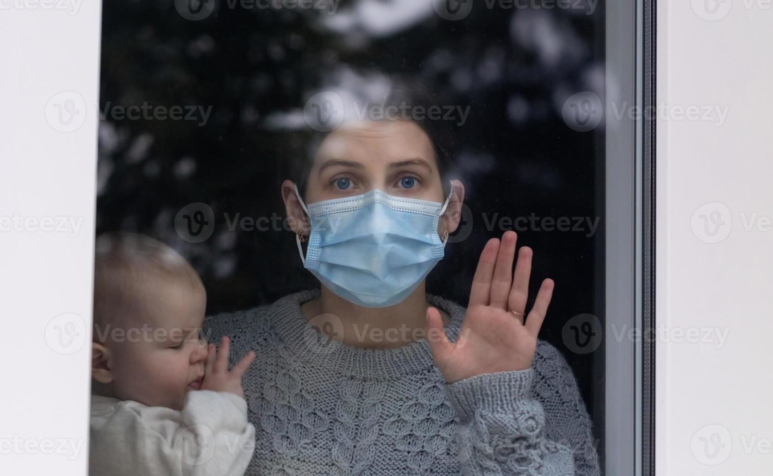 junge Mutter und Tochter schauen während einer Selbstisolationsquarantäne aus dem Fenster foto