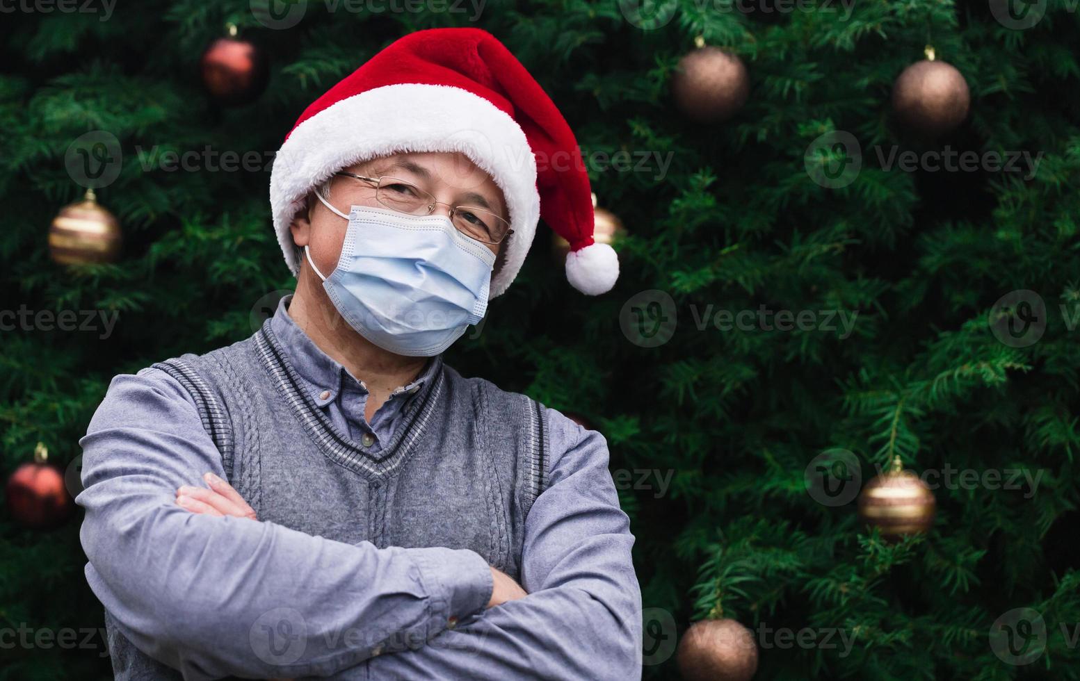 Nahaufnahmeporträt des älteren Mannes, der einen Weihnachtsmannhut und eine medizinische Maske mit Emotion trägt foto