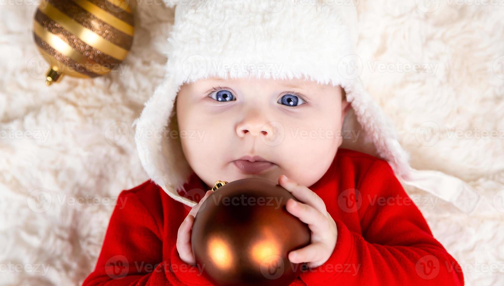 süßes Baby beißt Weihnachtsball auf dem Boden liegend foto