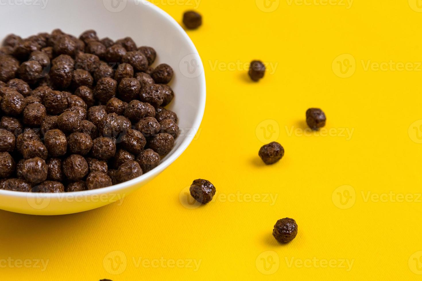 weiße Schüssel mit Schokoladenmais-Müslikugeln und Milch auf gelbem Hintergrund foto