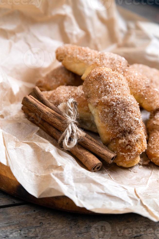 frische Croissants mit Zimt auf zerknittertem Papier auf hölzernem Hintergrundtisch foto