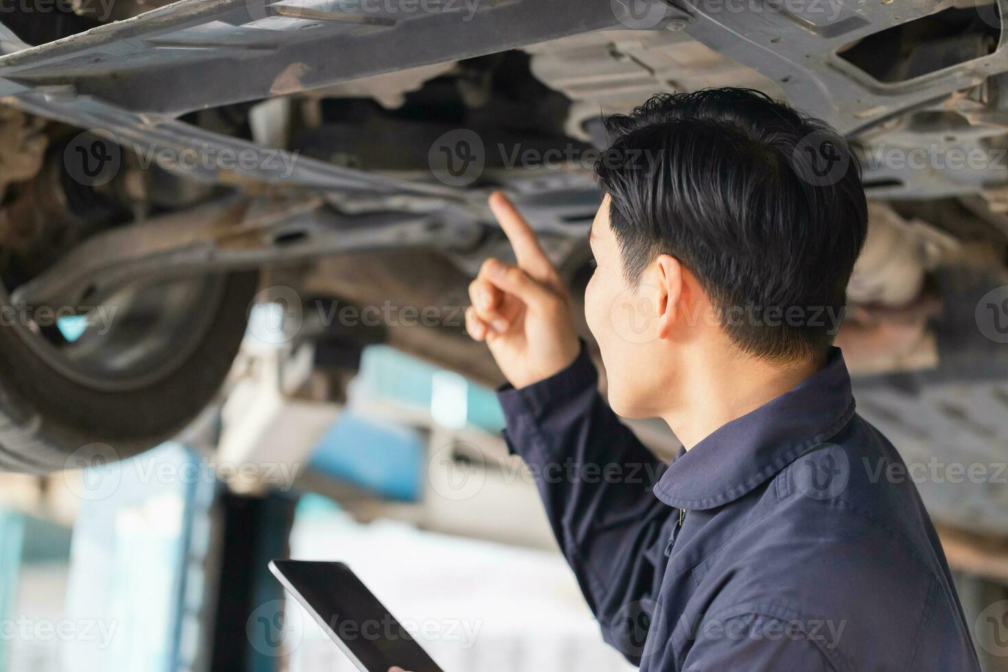 Auto Mechaniker Arbeiten im Garage, Techniker Mann Arbeiten im Auto Bedienung mit angehoben Fahrzeug, Auto Reparatur, und Instandhaltung foto