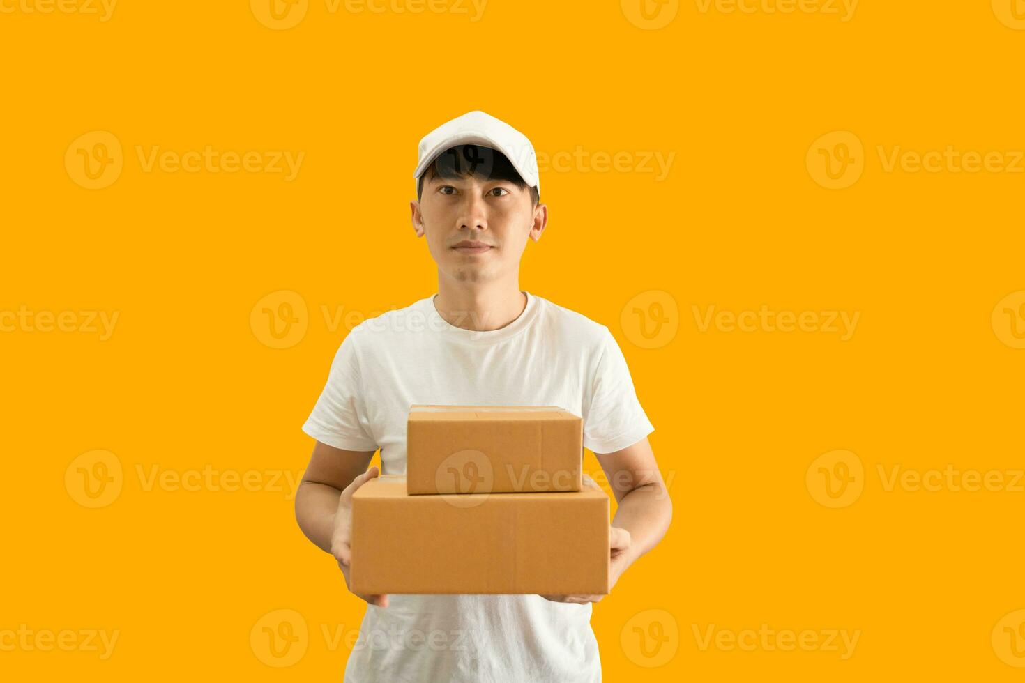 jung asiatisch Lieferung Mann tragen Deckel und Weiß leer T-Shirt halten Paket Post Box isoliert auf Gelb Hintergrund. ausdrücken Lieferung Bedienung Konzept. foto