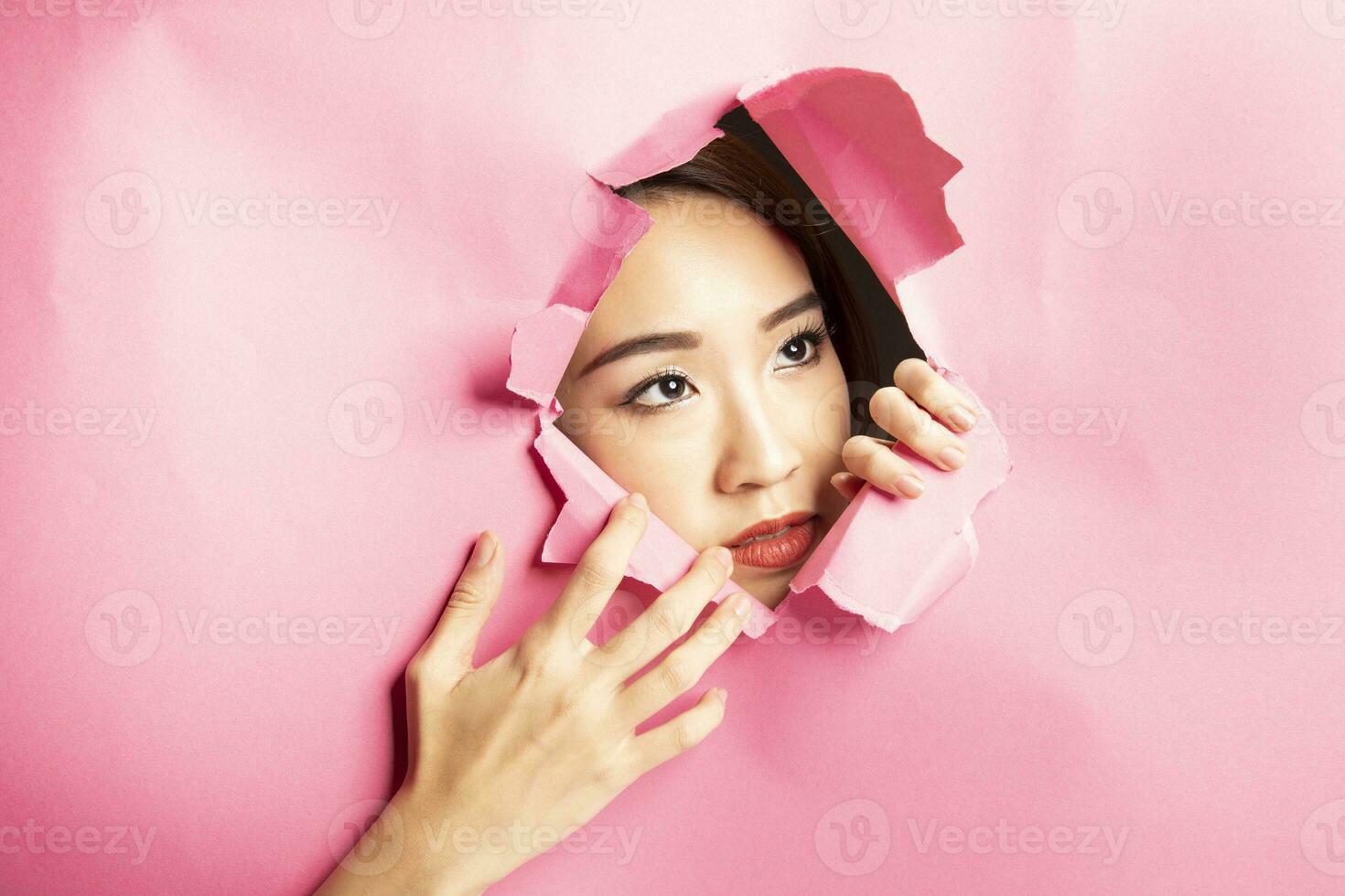 jung schön asiatisch Frau Ausdruck durch zerrissen Papier Loch foto