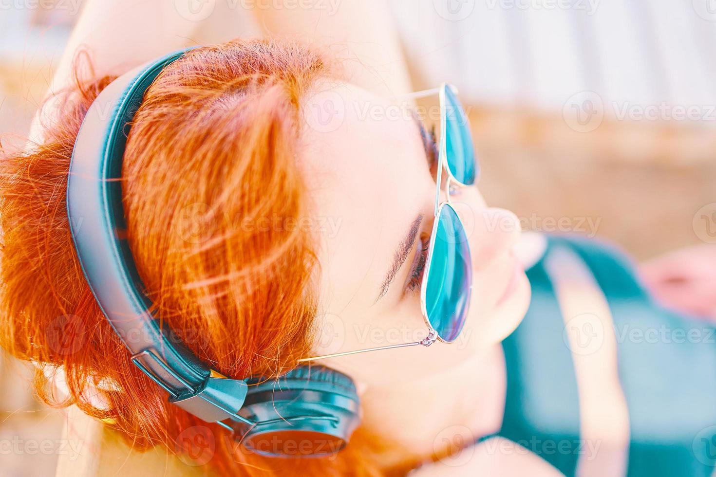 schöne Frau in der Sonnenbrille, die Musik am Strand hört foto