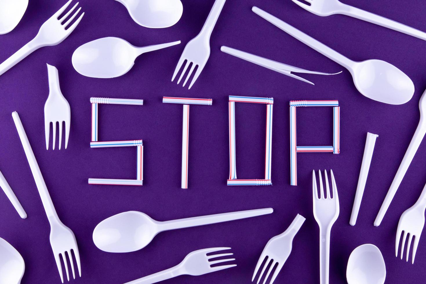 das Wort Stop aus Plastikröhrchen auf lila Hintergrund mit Plastikutensilien foto