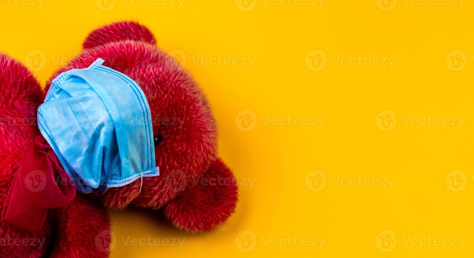 einsamer roter Teddybär in einer medizinischen Schutzmaske auf gelbem Grund foto